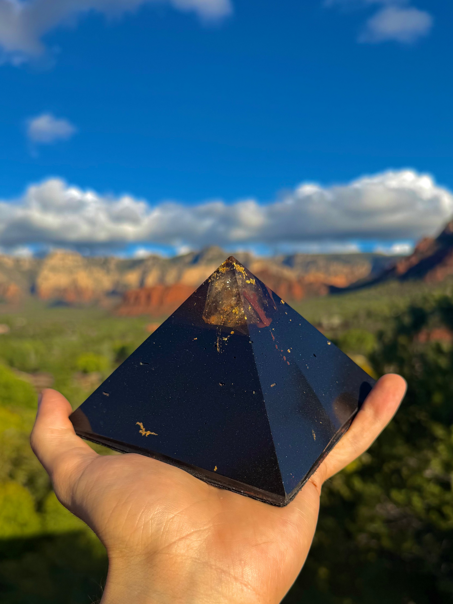 Person holding a pyramid-shaped stone with a scenic background of mountains and trees.