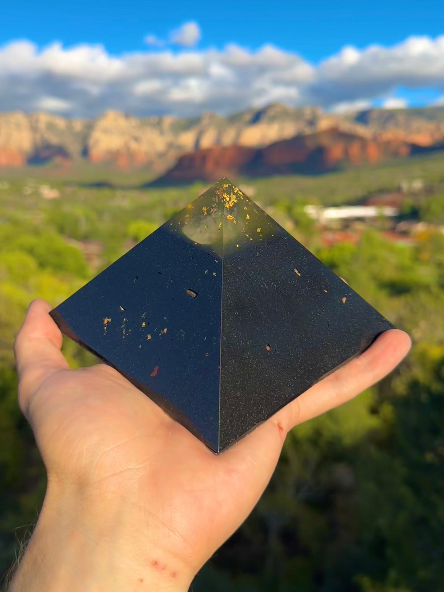 Person holding a black pyramid-shaped object with a scenic landscape in the background