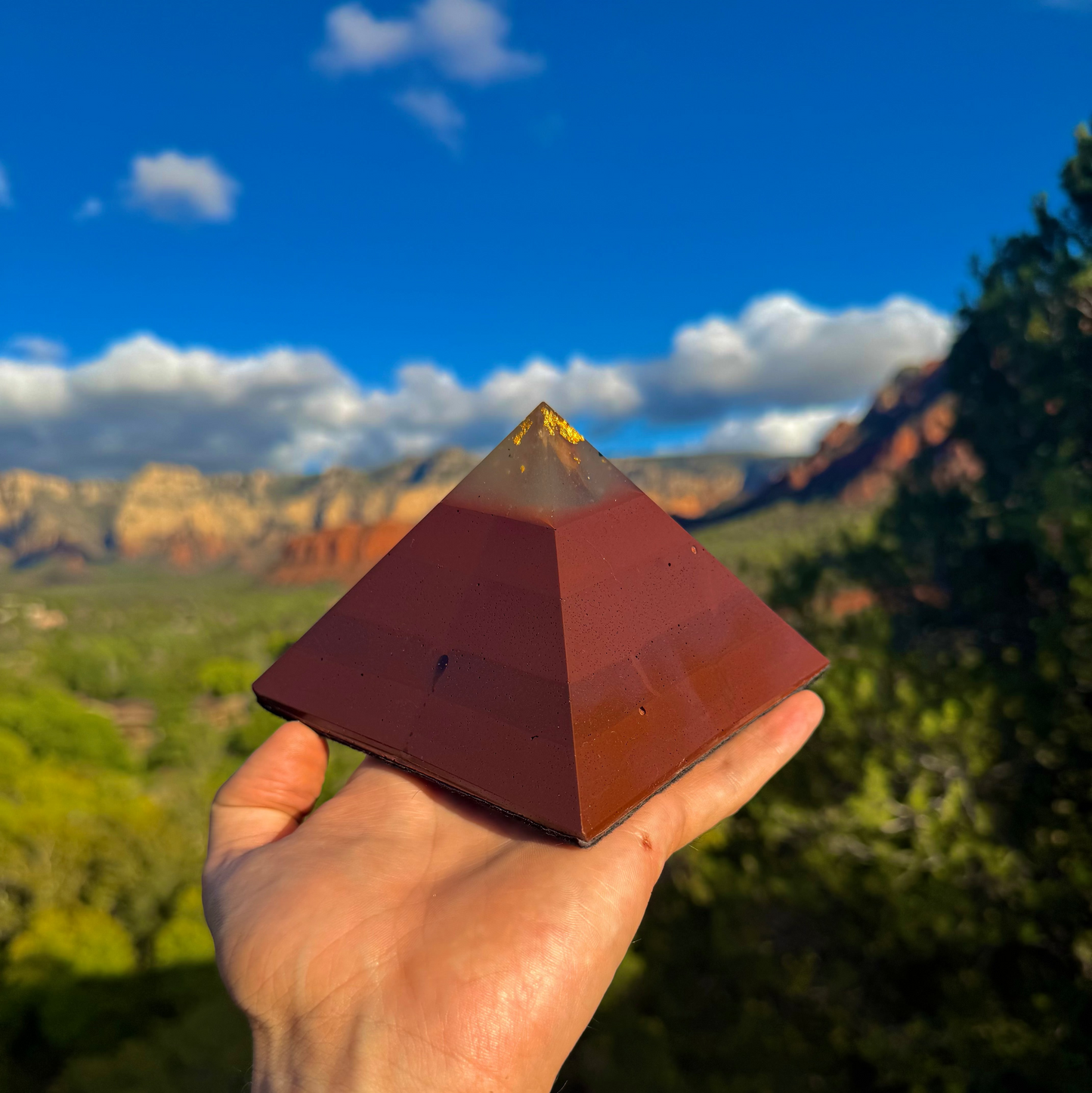 Pyramid-shaped object held in a hand with a scenic background of mountains and trees.