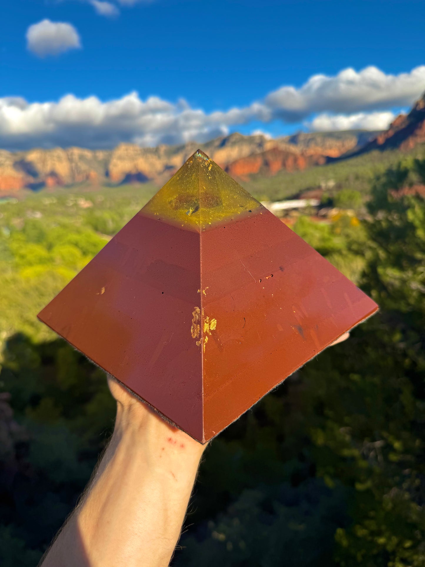 Pyramidal object held in front of a scenic landscape with mountains and greenery.
