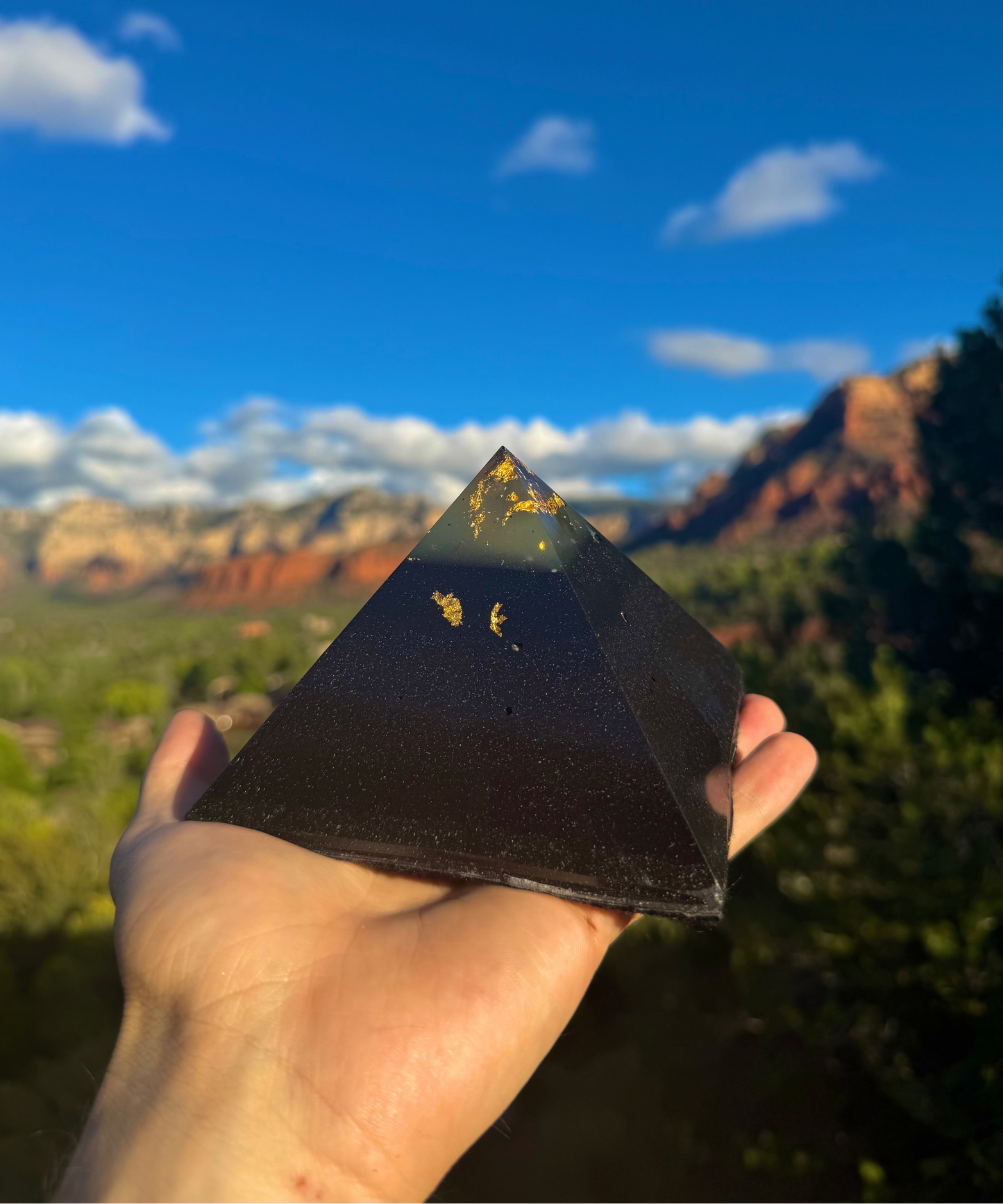 Pyramid-shaped object held in a hand with a scenic background of mountains and blue sky.