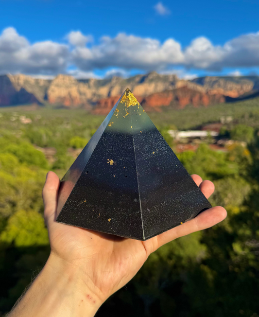 Person holding a black pyramid crystal with a scenic landscape in the background