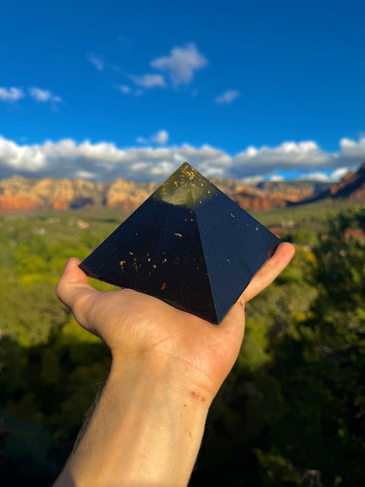 Person holding a black pyramid crystal with a scenic landscape in the background
