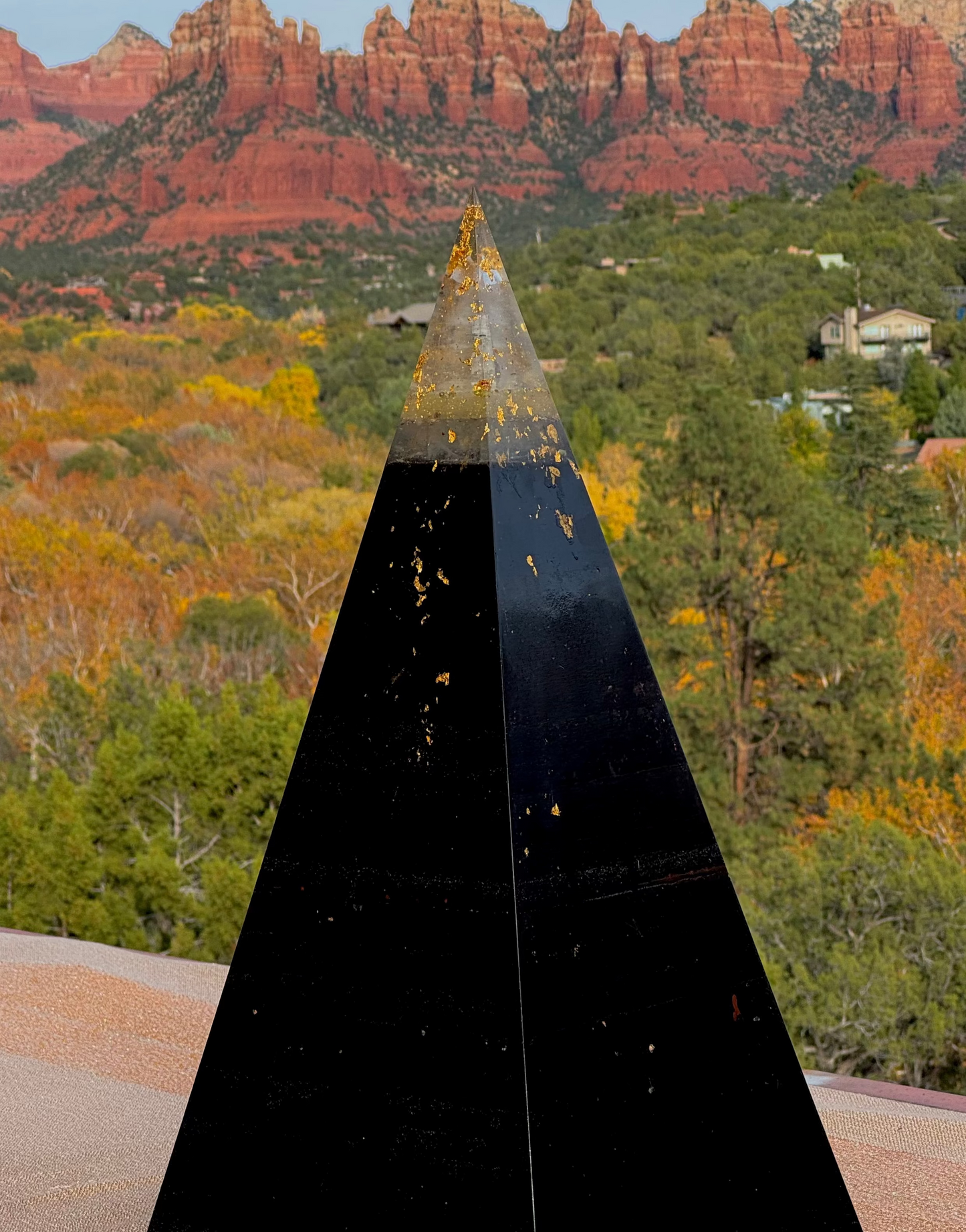 Black pyramid-shaped object with a scenic background of red rock formations and green trees.